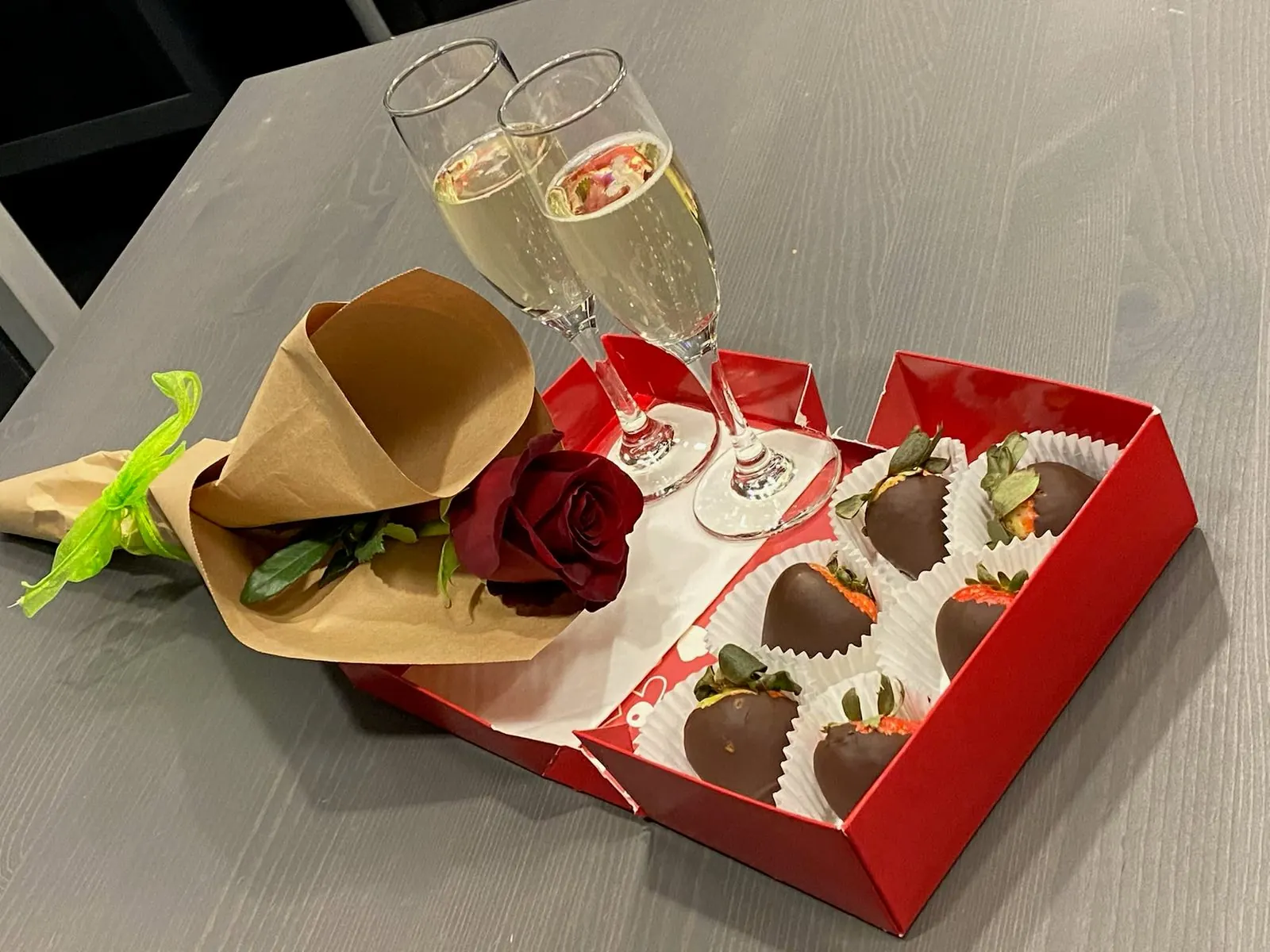 Box of chocolate covered strawberries with a rose and a glass of champagne